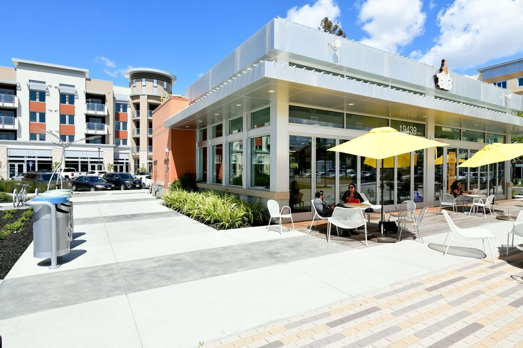 a large white building with people sitting at tables under umbrellas outside Main Street Lofts Cupertino