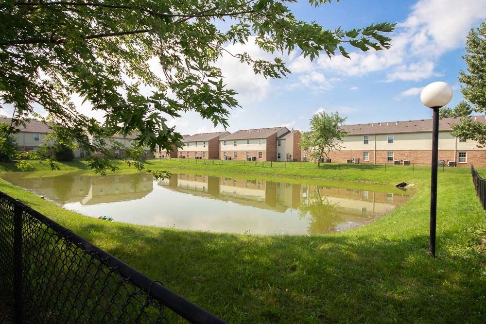 Pond in the middle of a grassy area with apartment buildings in the background at Maple Tree Apartments in LaPorte, IN