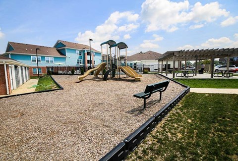 A playground with a yellow slide and a green bench.