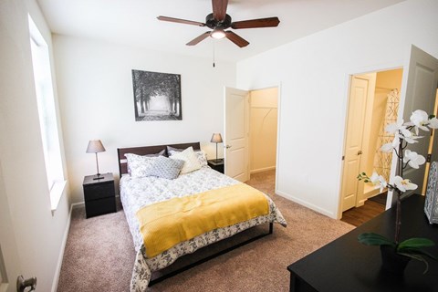 A bedroom with a bed, a ceiling fan, and a painting on the wall.