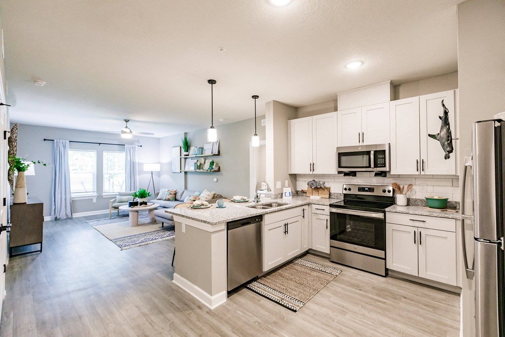 an open kitchen and living room with white cabinets and stainless steel appliances