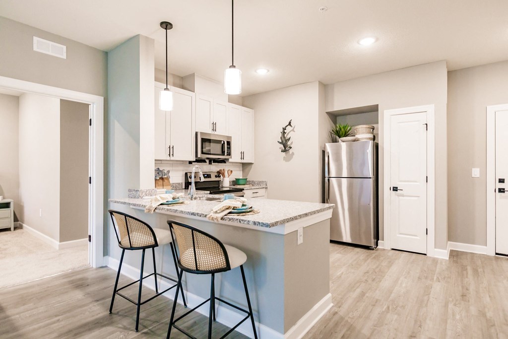 an open kitchen with a counter with three stools and a stainless steel refrigerator