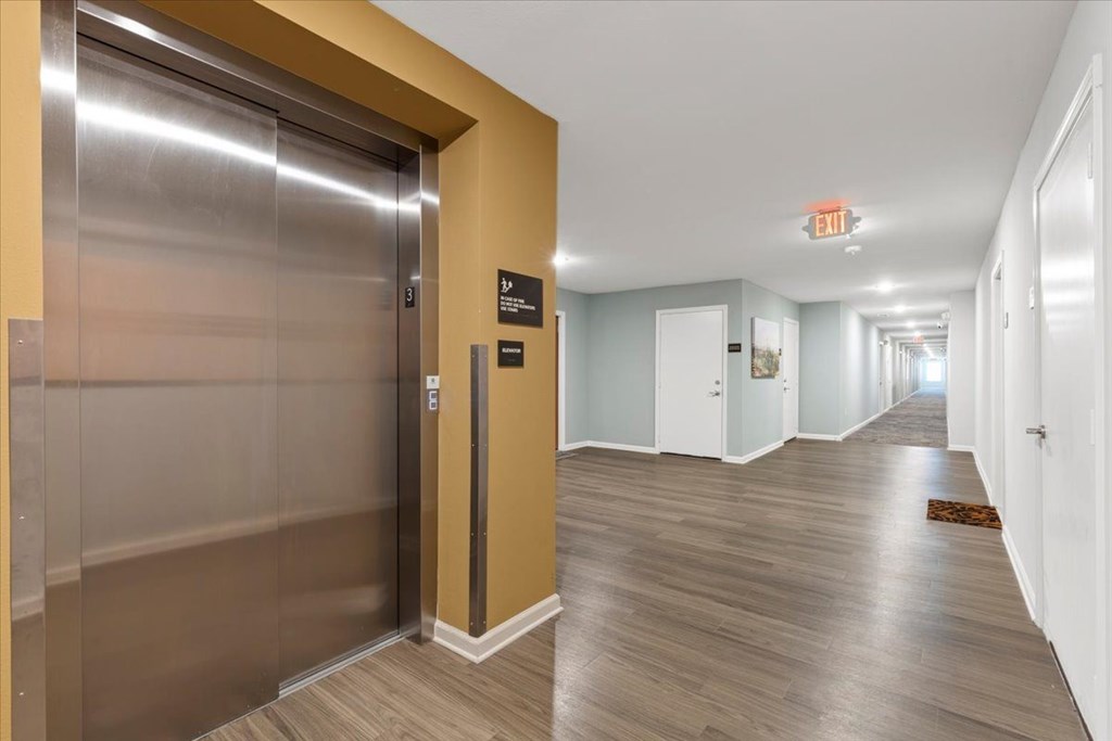 A long hallway with a silver elevator on the left.