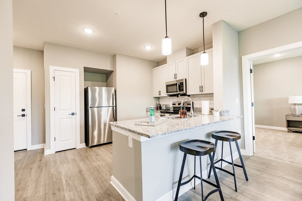 a kitchen with a large island with bar stools and a stainless steel refrigerator