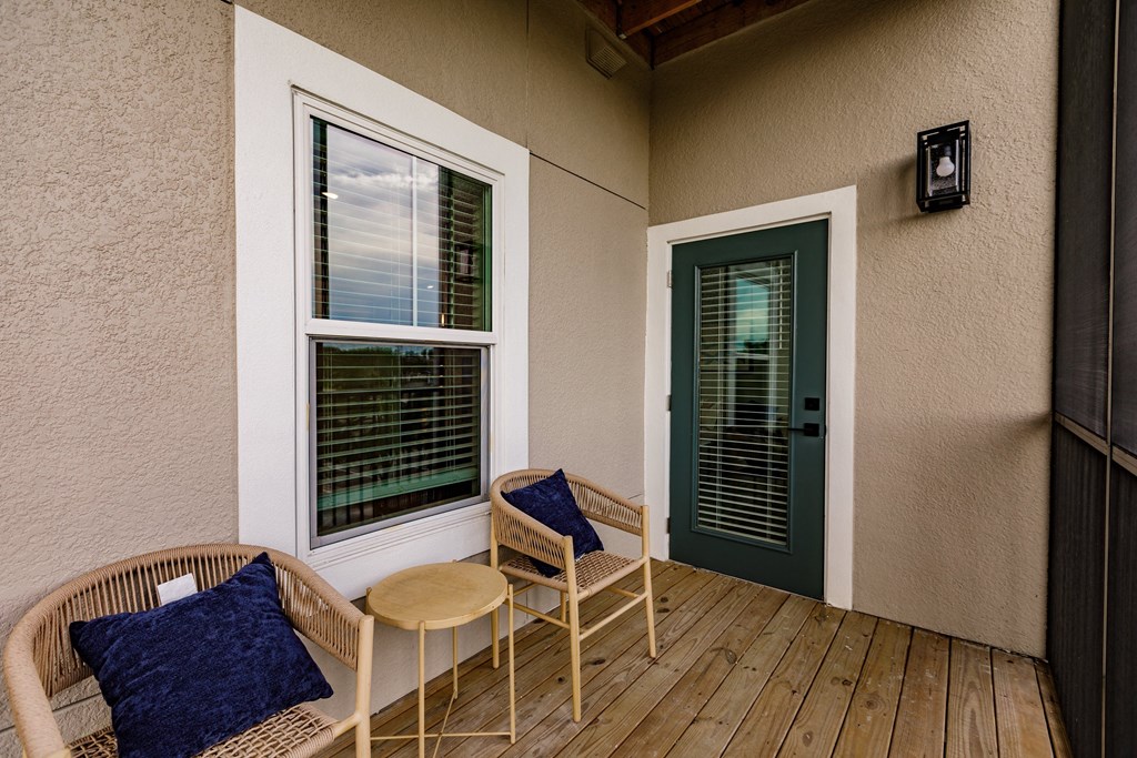 a porch with two chairs and a table and a green door