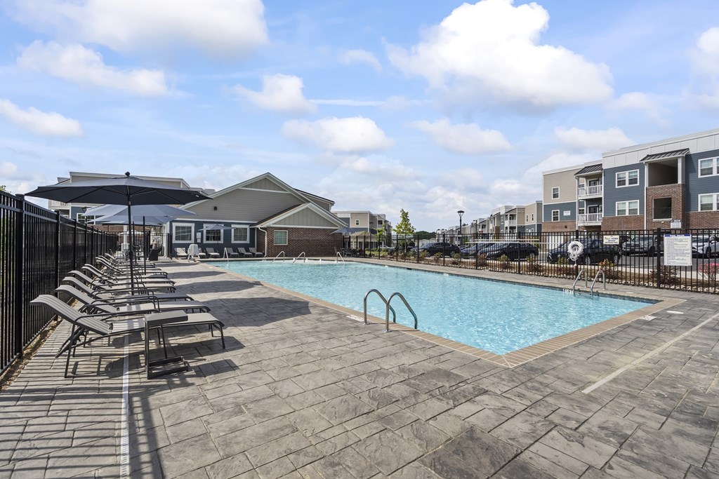 A swimming pool surrounded by a black fence and lounge chairs.