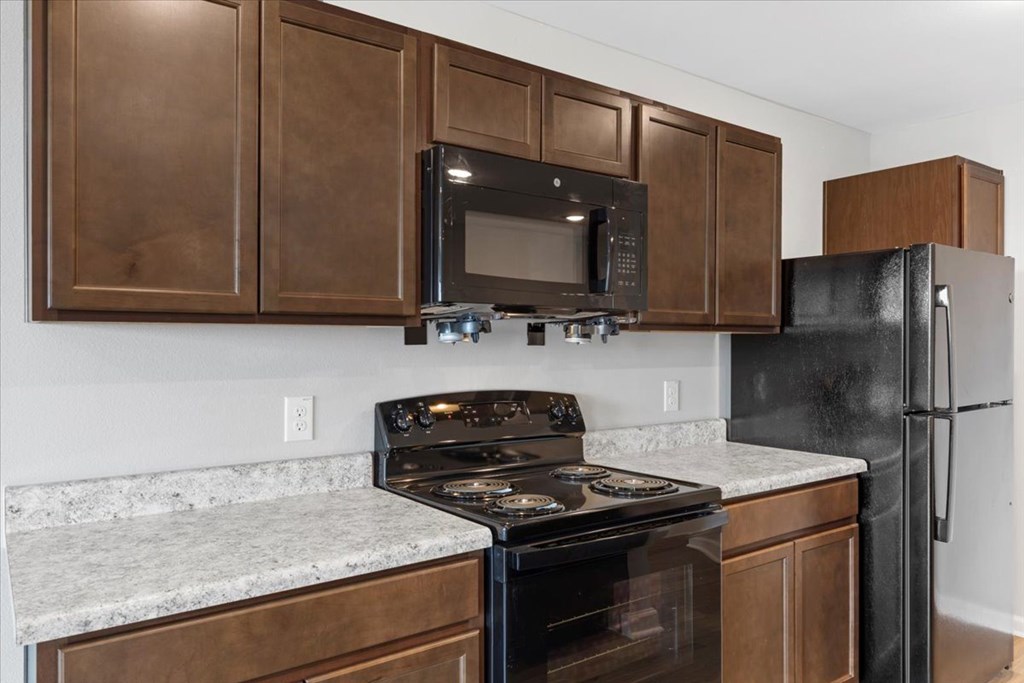 A kitchen with a black refrigerator, black stove, and black microwave.