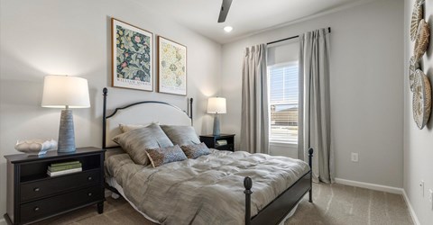 A bedroom with a large bed, a nightstand with a lamp, and two wall art pieces.