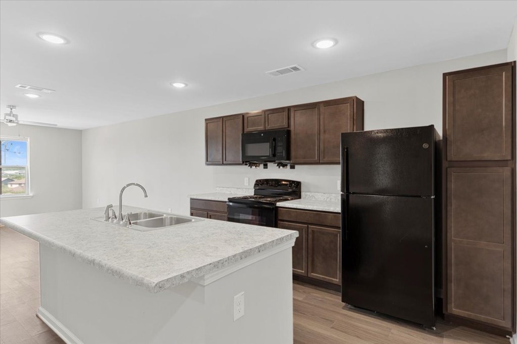 A kitchen with a black refrigerator and brown cabinets.