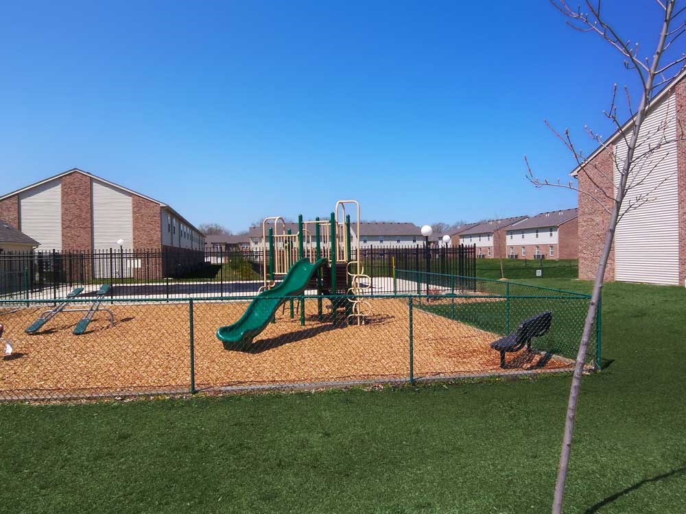Playground with a slide and monkey bars inside a fenced area at Maple Tree Apartments in LaPorte, IN