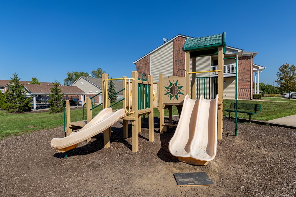 A playground with a slide and a green roofed building in the background.