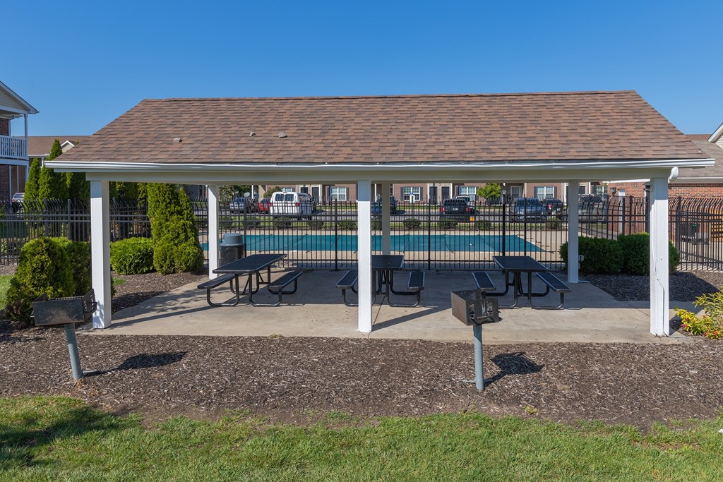 A covered picnic area with tables and benches is set up in a park.