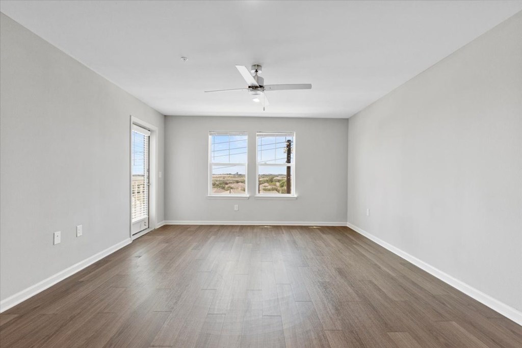 A spacious room with a ceiling fan and two windows.