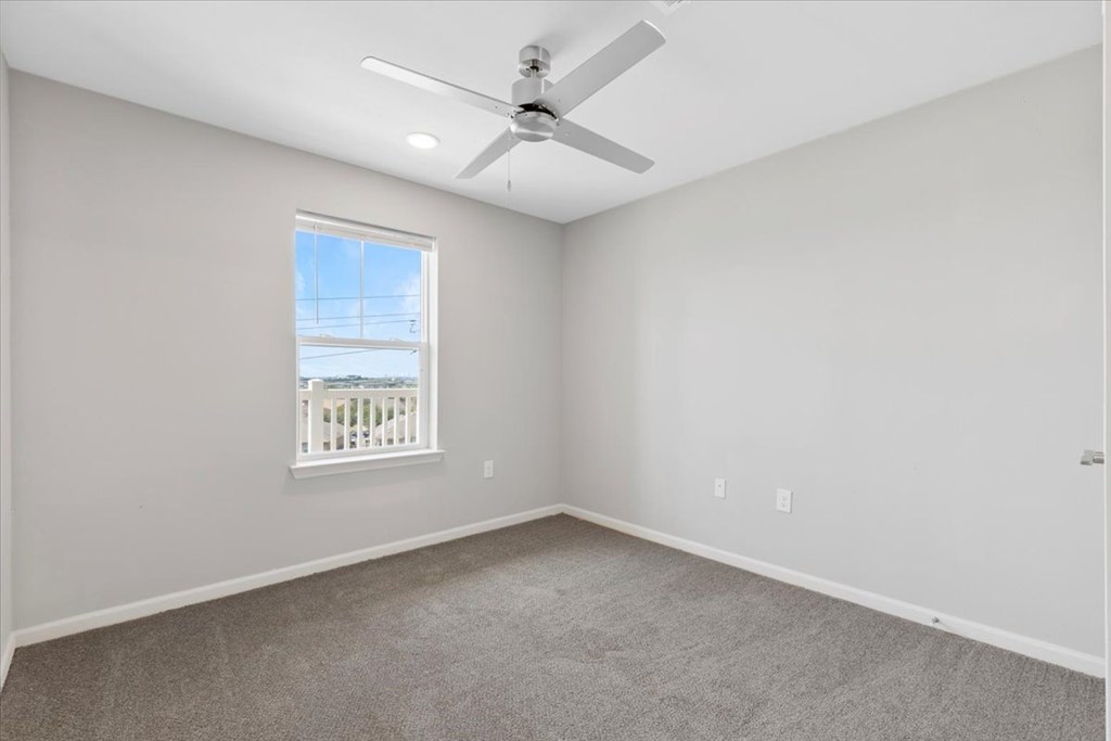 A room with a ceiling fan and a window overlooking a deck.