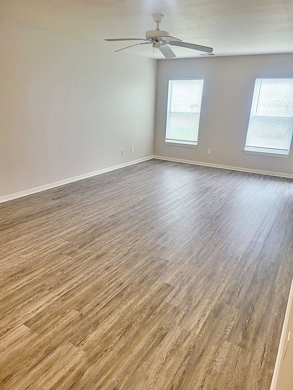 an empty living room with wood floors and a ceiling fan