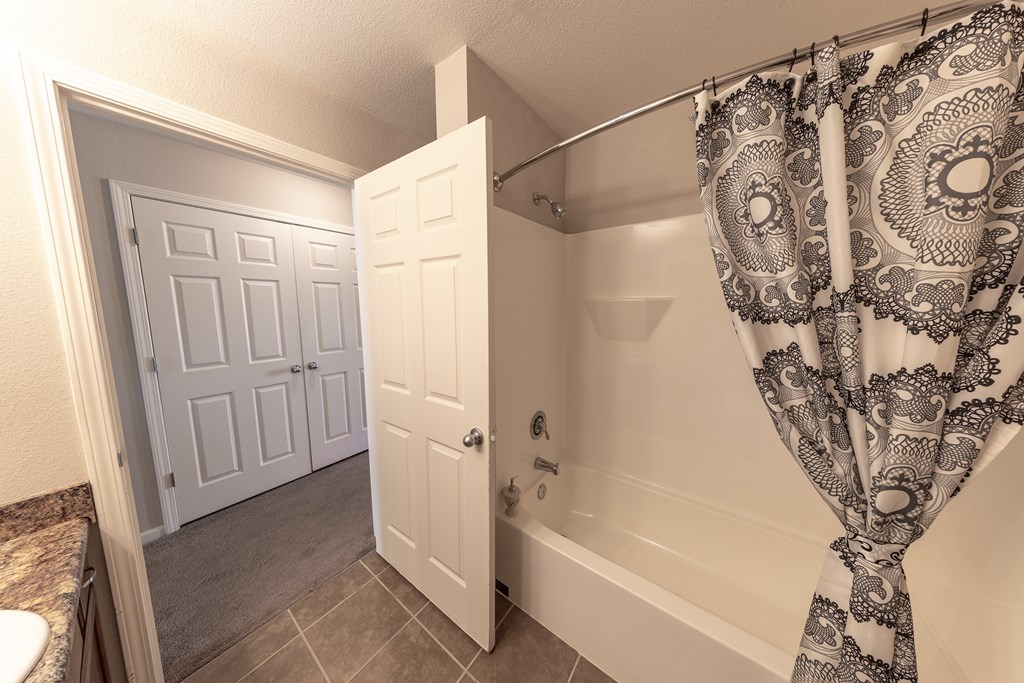 A bathroom with a bathtub, shower curtain, and two doors.