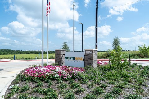 A sign for Northwind stands in front of a road with a flagpole and flowers.