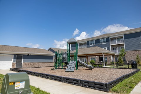 A playground with a green slide and a sandbox in front of a building.