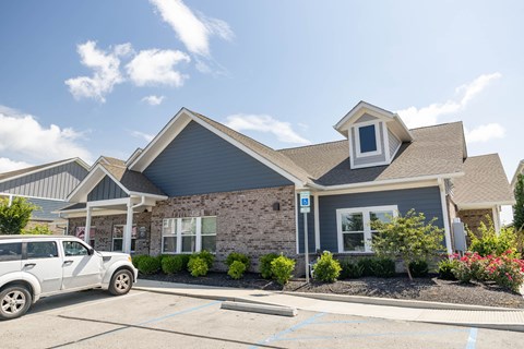 A white car is parked in front of a grey house.