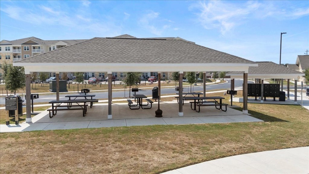 A covered picnic area with benches and a playground in the background.