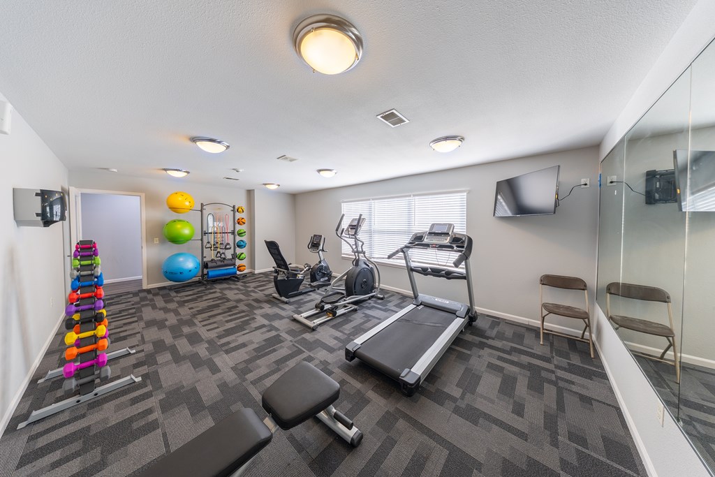 A spacious gym with a variety of equipment including a treadmill, exercise balls, and dumbbells.
