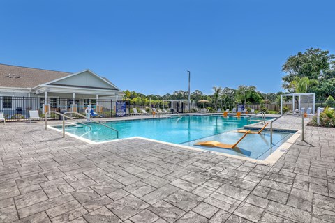 A large outdoor swimming pool with a sun lounger and a building in the background.