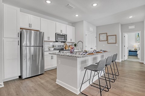 A kitchen with a refrigerator, microwave, and a counter with chairs.