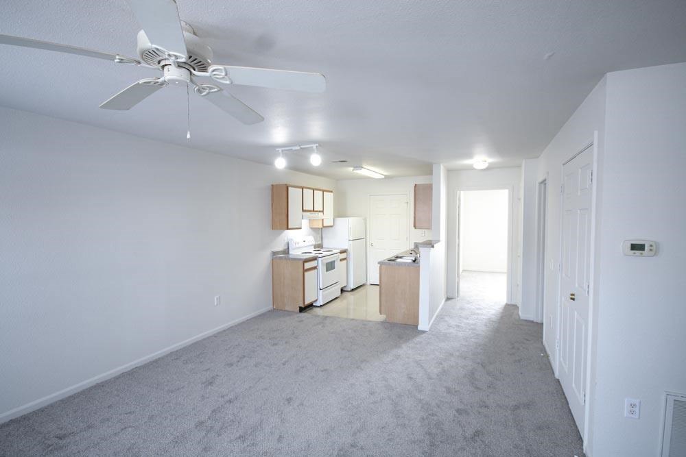 A spacious living room with a ceiling fan and built-in kitchenette.