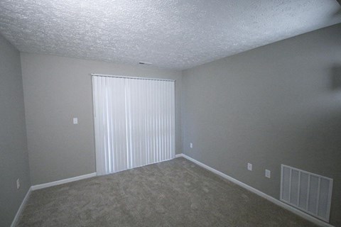 Empty living room with a large window and white blinds at Canterbury House apartments in Tipton, Indiana
