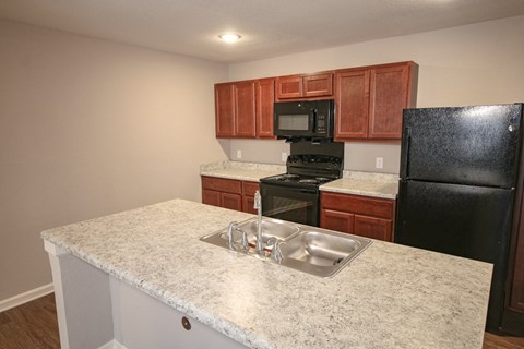 A kitchen with a black refrigerator and brown cabinets.