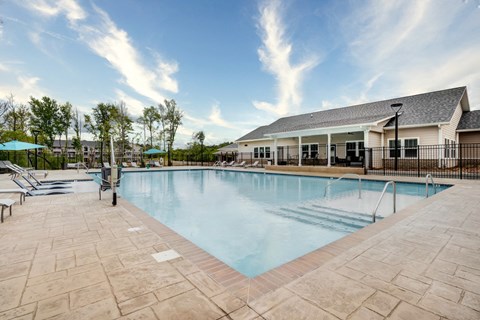 Swimming pool at Aurora Luxury Apartments with chaise lounge chairs and a building in the background