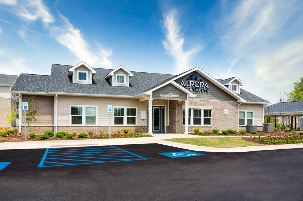 Aurora Apartments clubhouse building  with a gray roof and blue handicapped parking spaces