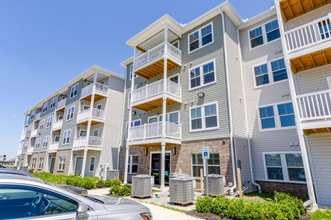 A row of modern apartment buildings with balconies and a car parked in front.