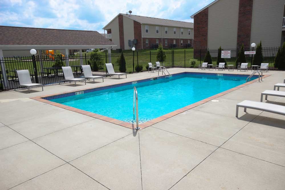 A large swimming pool surrounded by a black fence and lounge chairs.