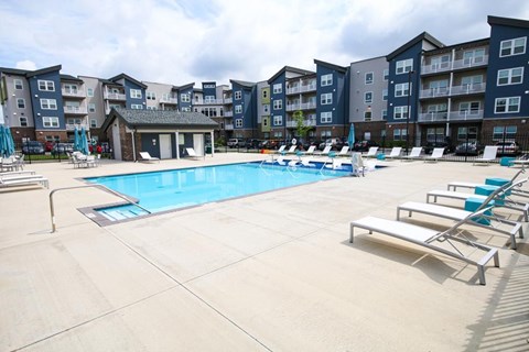 A large swimming pool surrounded by lounge chairs in front of apartment buildings.