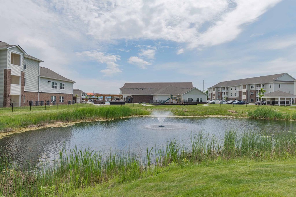 A pond with a fountain with grove city apartments in the background