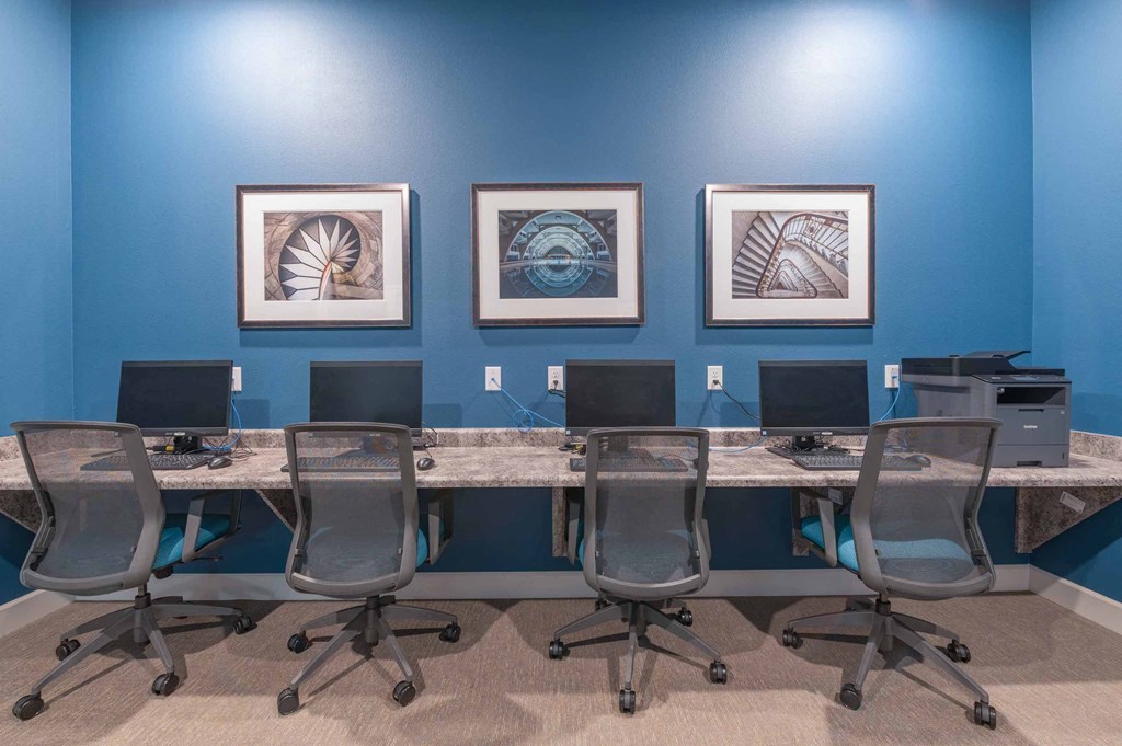 a desk with computers and chairs in front of a blue wall