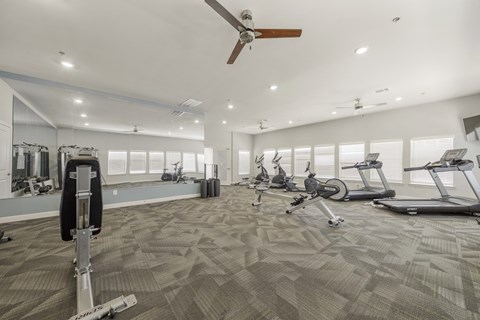 A spacious gym with a variety of exercise equipment and a ceiling fan.