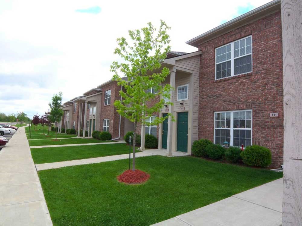 A tree in the middle of a grassy area in front  apartment building at Canterbury House apartments in Warsaw, IN