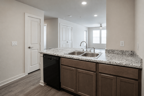 A kitchen with a black dishwasher and brown cabinets.