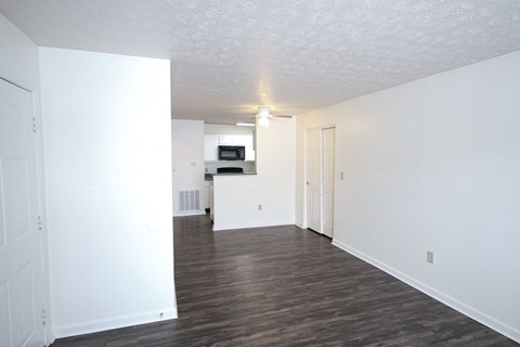 an empty living room and kitchen with white walls and wood flooring