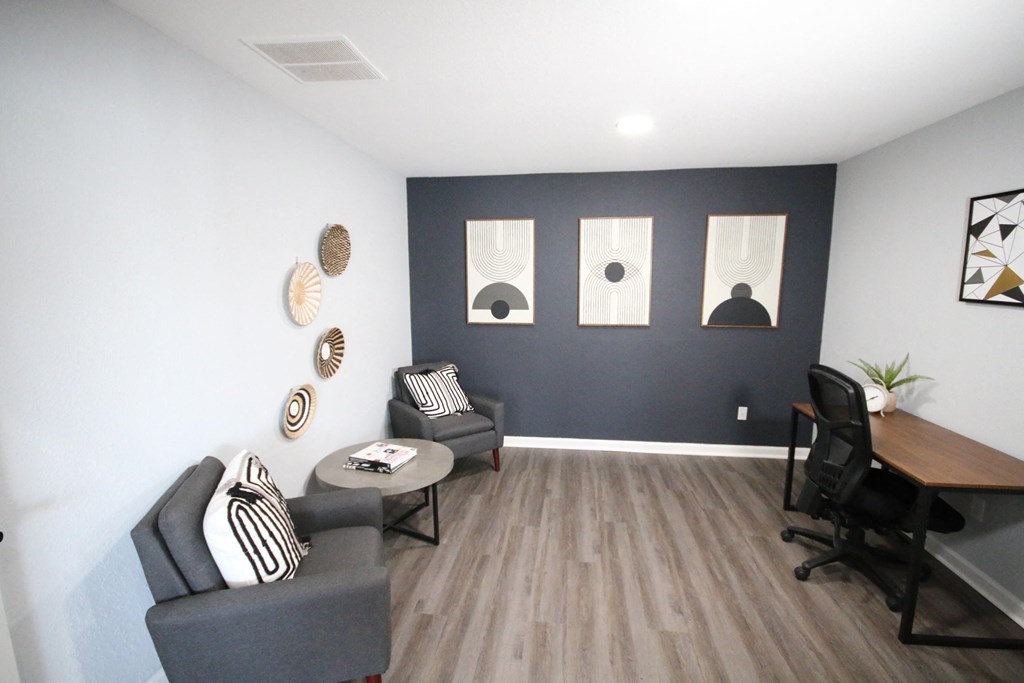 A room with a grey sofa, a black chair, a grey table and a wooden desk.