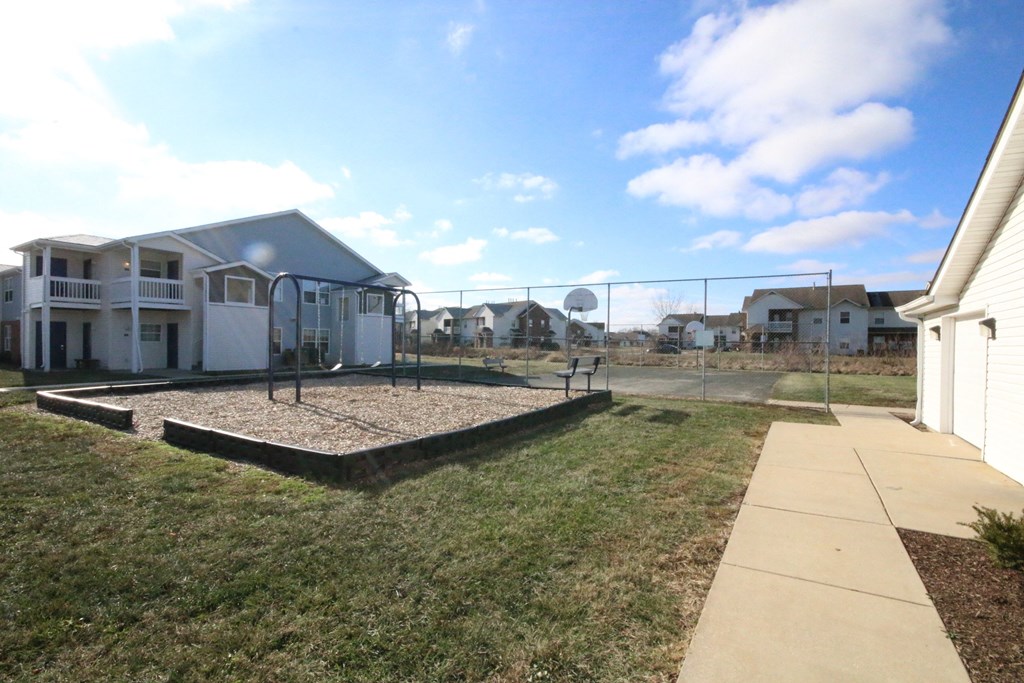A playground area with a slide and a swing set in a grassy yard.