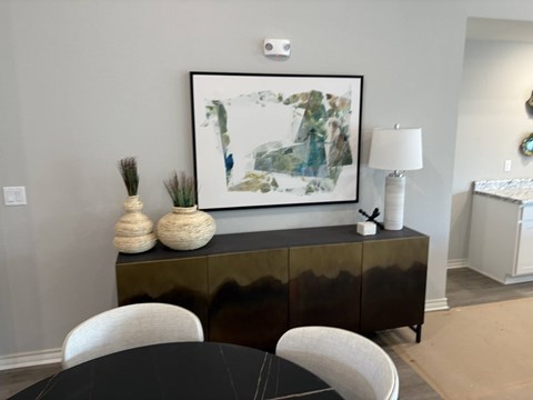 A black and white painting hangs above a black cabinet with a white vase and a white lamp on top.