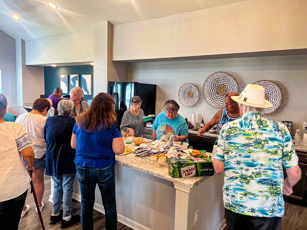 a group of people standing around a counter preparing food in a kitchen