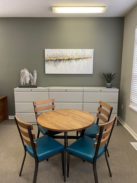 A grey wall with a painting and a table with four chairs.