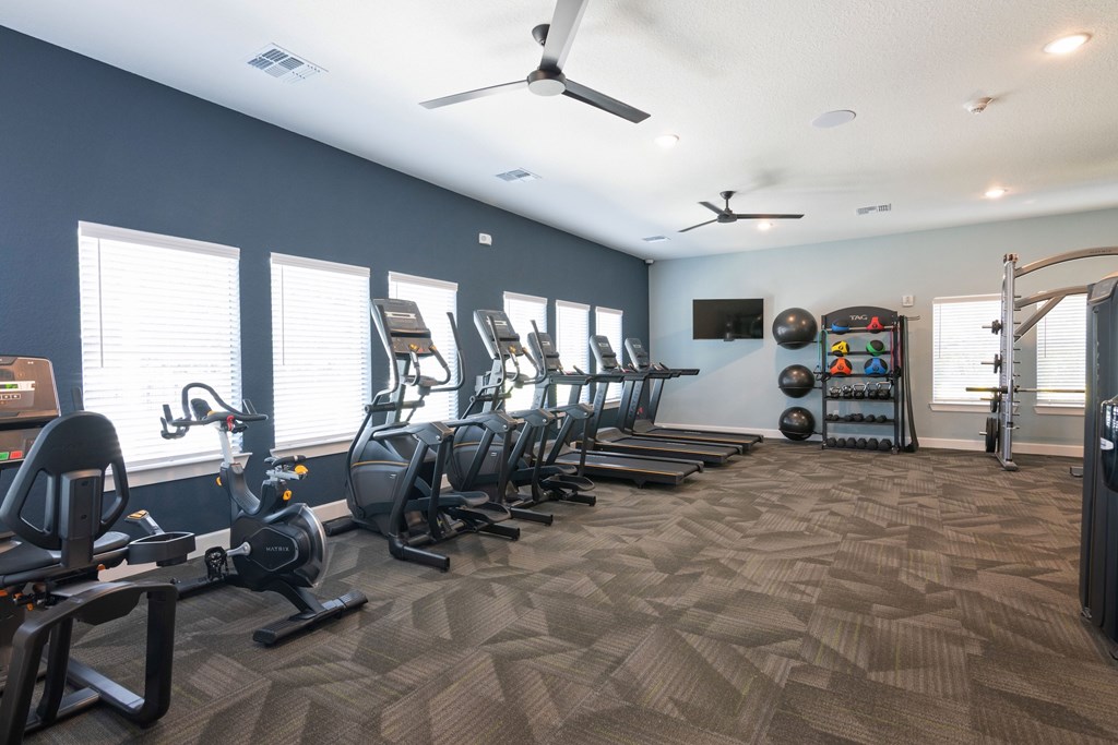 A spacious gym with a variety of exercise equipment and a ceiling fan.