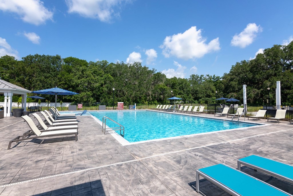 A pool surrounded by trees and chairs.