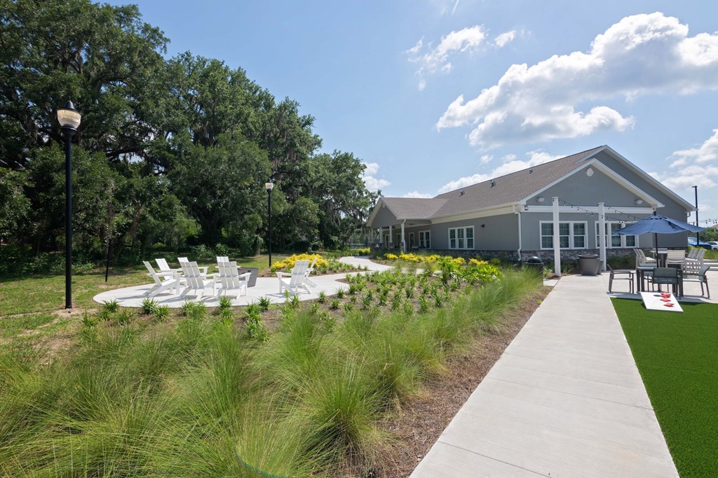 A building with a grey roof and white windows is surrounded by a grassy area and trees.
