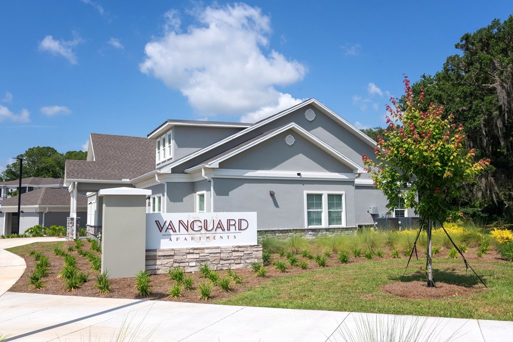 A Vanguard Apartments sign is in front of a grey building.